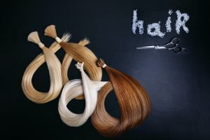 hair extensions of four colors on a dark background with scissors. copyspace. top view