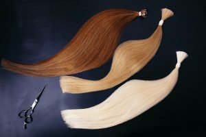 hair extensions of three colors on a dark background with scissors. copyspace. top view